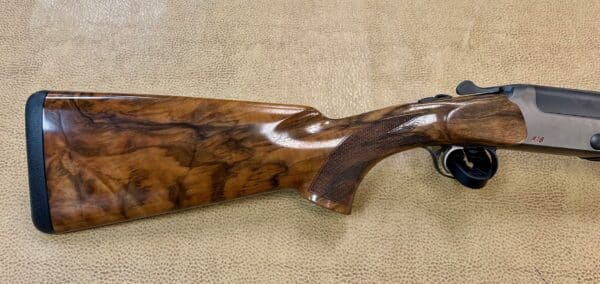 A well-crafted shotgun with a walnut stock and matte metal finish resting on a textured surface.