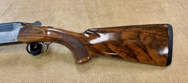 Overhead view of a shotgun with a wooden stock and silver barrel on a textured background.