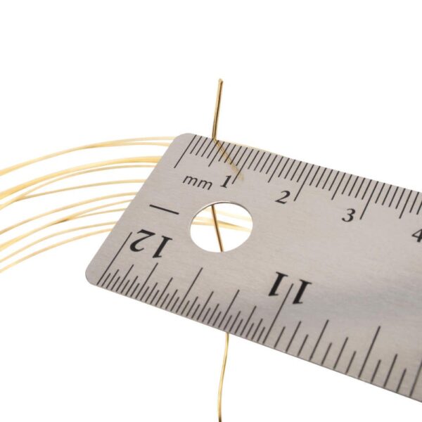 A close-up of a metallic ruler with measurements, next to a thin, golden wire, showing the wire's fine detail and structure.