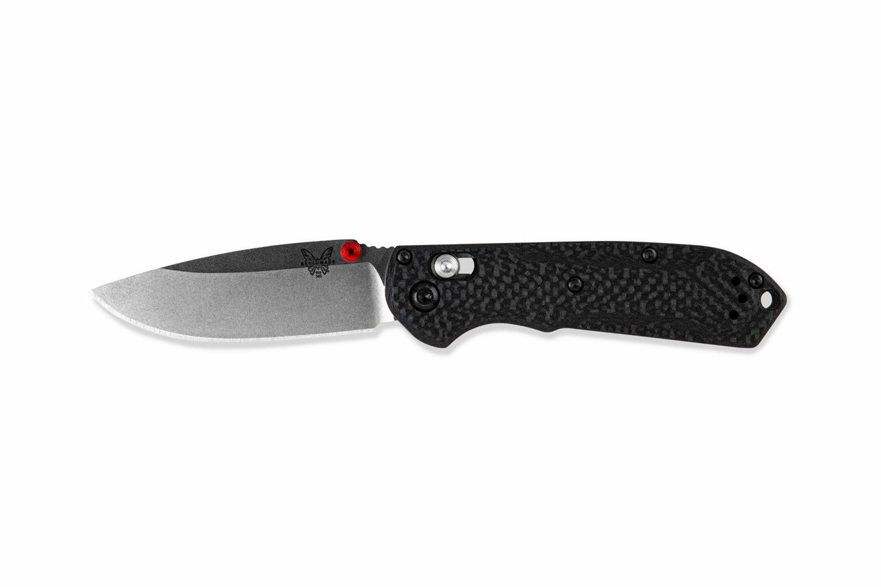 A black Benchmade folding knife with a silver blade, red thumb stud, and a carbon fiber-textured handle, resting on a white background.