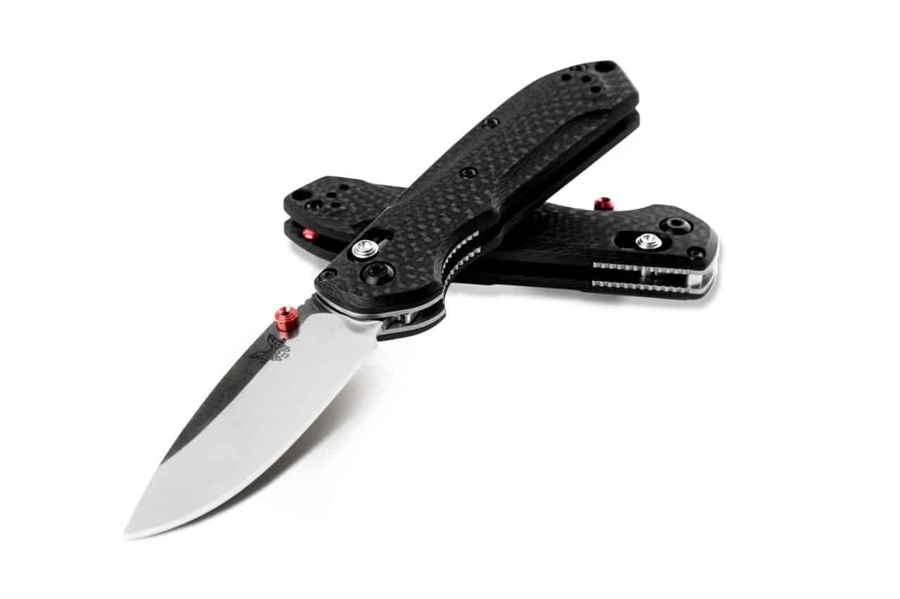 BENCHMADE MINI-FREEK - Two black and silver folding knives with carbon fiber handles, one open and one closed, isolated on white. The open knife is in the foreground with the blade extended, showing a silver steel blade with the Benchmade butterfly logo, and red accent pins. The closed knife rests behind, also showing red accent pins.