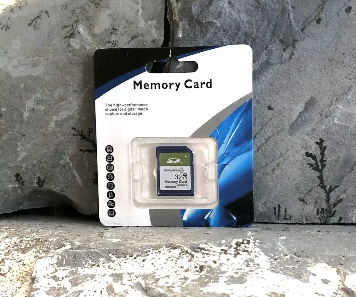 RECONECO OUTDOORS 32GB SD CARD - A 32GB SD memory card displayed in its packaging, showcasing digital storage for image capture. Background features textured stone.