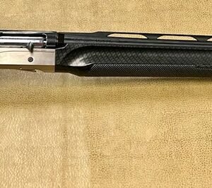 A modern shotgun with a carbon fiber pattern on stock and forend, displayed on a beige surface.