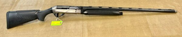 A modern shotgun with a carbon fiber pattern on stock and forend, displayed on a beige surface.