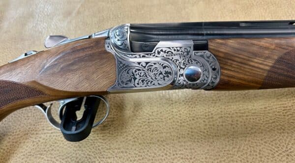 Close-up of a Beretta shotgun with intricately engraved silver metalwork and polished wooden stock.