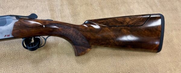 A close-up of a polished wooden shotgun stock with intricate grain patterns on a textured background.