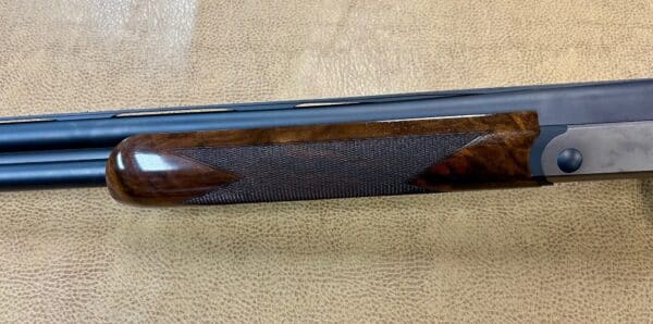 Close-up of a double-barreled shotgun's side with wooden stock on textured background.