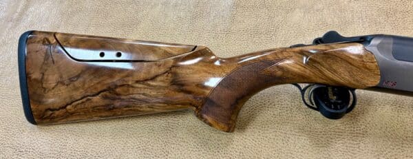 A wooden shotgun stock with detailed grain and a textured grip against a textured fabric background.