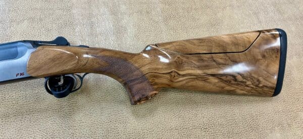 A close-up of a shotgun's wooden stock and metal barrel, resting on textured fabric.