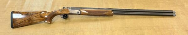 A side view of an over-under double-barrel shotgun with a wooden stock on a textured background.