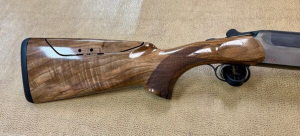 A shotgun with a wooden stock and grey barrel resting on a textured surface.