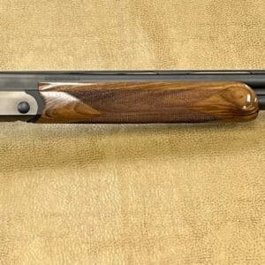 Over-under shotgun with wooden stock and polished barrels on a textured background.