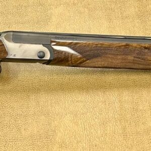 Side view of an over-under shotgun with wooden stock on a textured background.