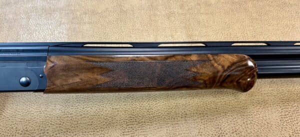 Close-up of a shotgun's wooden stock and metal barrel against a textured background.