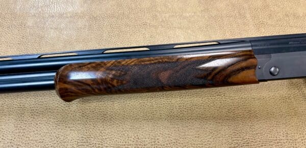 Close-up of a shotgun with a wooden stock and steel barrel on a textured background.