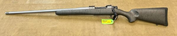 A stainless steel bolt-action rifle with a synthetic stock and attached price tag on a beige background.