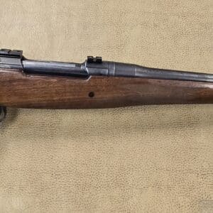 A wooden hunting rifle with a scope on a textured background.