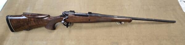 A wooden hunting rifle with a scope on a textured background.