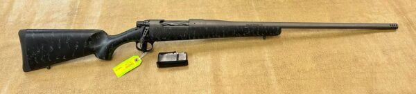 A black bolt-action rifle with a detachable kwik klip on a beige surface.