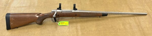 A bolt-action rifle with a wooden stock that has been engraved and a price tag displayed on a fabric background.