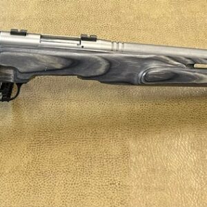 A bolt-action rifle with a gray laminated stock rests on a textured surface with a price tag.