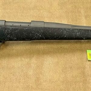 A black bolt action rifle with a price tag lying on a beige textured surface.