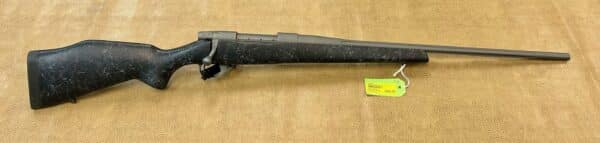 A black bolt action rifle with a price tag lying on a beige textured surface.