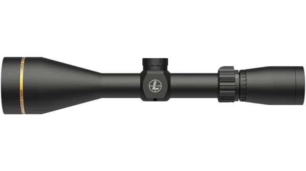 The image depicts a black riflescope with a cylindrical body, tapering towards the front. The objective lens is slightly wider, featuring a gold accent near the base. A central assembly contains a logo, with an adjustable zoom control on the right side that is marked with numerical values. The scope is designed for stability and precision in targeting. The lens caps are not visible, implying an open view for use.