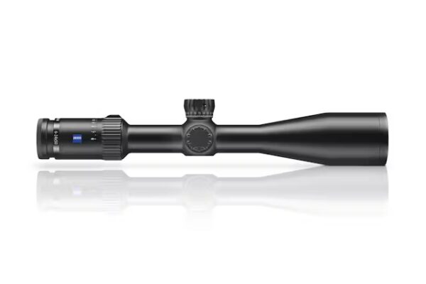 The image presents a black rifle scope with a matte finish, approximately two-thirds of the image length. The scope consists of a cylindrical body tapering towards the front, with an adjustable magnification ring on the left side, marked with incremental settings. A centrally located elevation knob indicates precision adjustments, while the rear end is slightly larger, showing an objective lens housing. The image is taken against a soft light, creating a subtle reflection beneath the scope, enhancing its sleek outline.