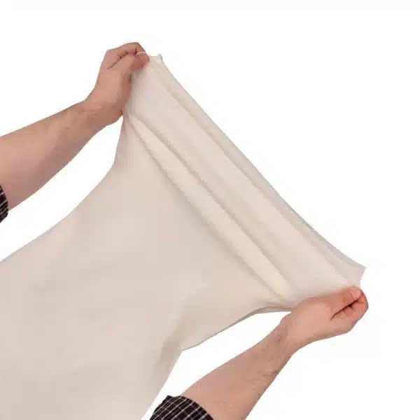 A person stretching a large, soft, cream-colored fabric, showcasing its elasticity and texture.